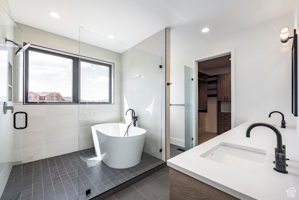 Bathroom featuring dual sinks, shower with separate bathtub, tile floors, and tile walls