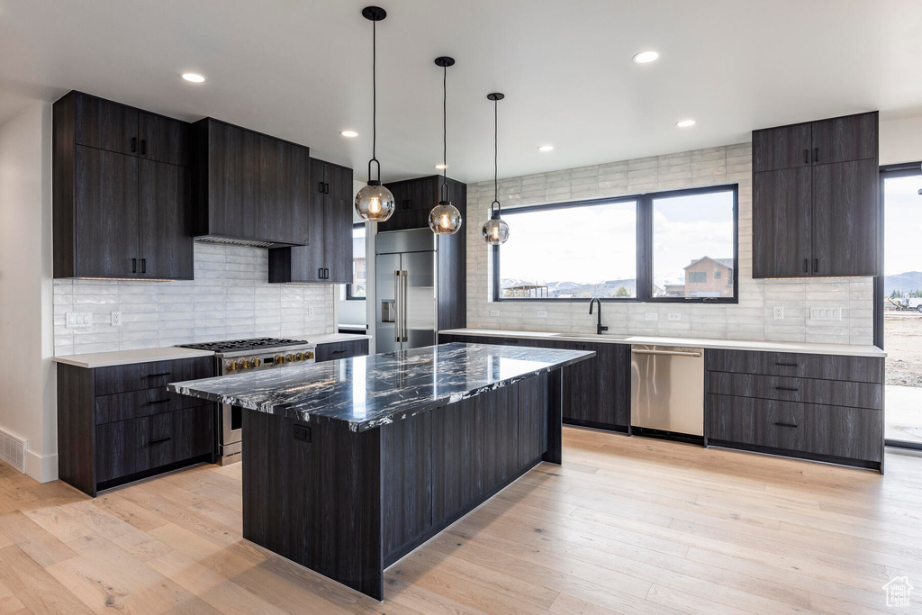 Kitchen with a kitchen island, backsplash, high end appliances, hanging light fixtures, and light hardwood / wood-style flooring