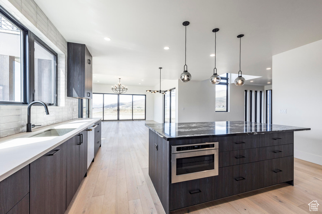 Kitchen with an inviting chandelier, a spacious island, light wood-type flooring, decorative light fixtures, and stainless steel oven