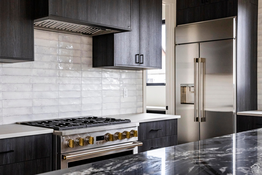 Kitchen with decorative backsplash, dark brown cabinetry, premium appliances, and custom range hood