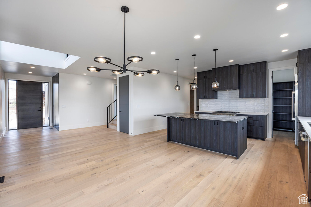 Kitchen featuring a large island, dark stone counters, light wood-type flooring, pendant lighting, and decorative backsplash