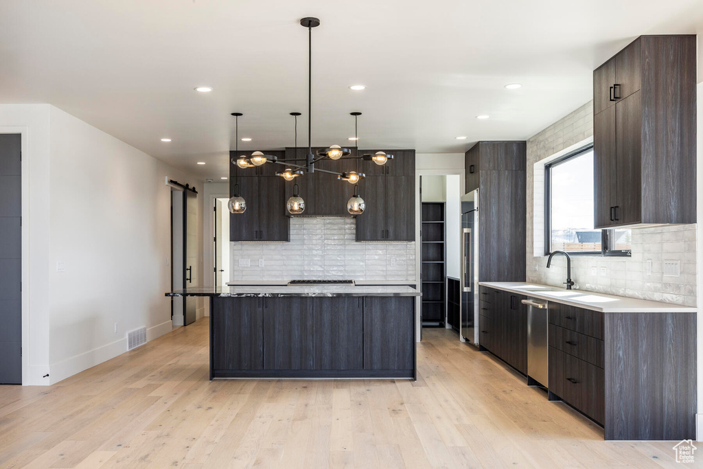 Kitchen featuring a barn door, a kitchen island, tasteful backsplash, hanging light fixtures, and light hardwood / wood-style flooring