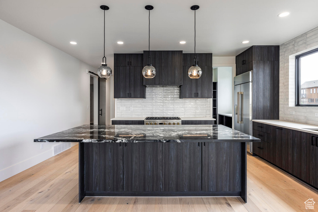 Kitchen featuring backsplash, light hardwood / wood-style floors, range, pendant lighting, and a center island