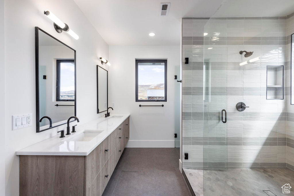 Bathroom featuring a shower with door, tile floors, and double sink vanity