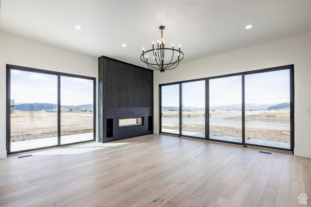 Unfurnished living room with a water and mountain view, a chandelier, a large fireplace, and light hardwood / wood-style flooring