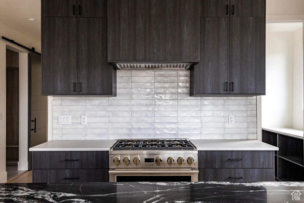 Kitchen featuring a barn door, high end range, custom exhaust hood, and tasteful backsplash