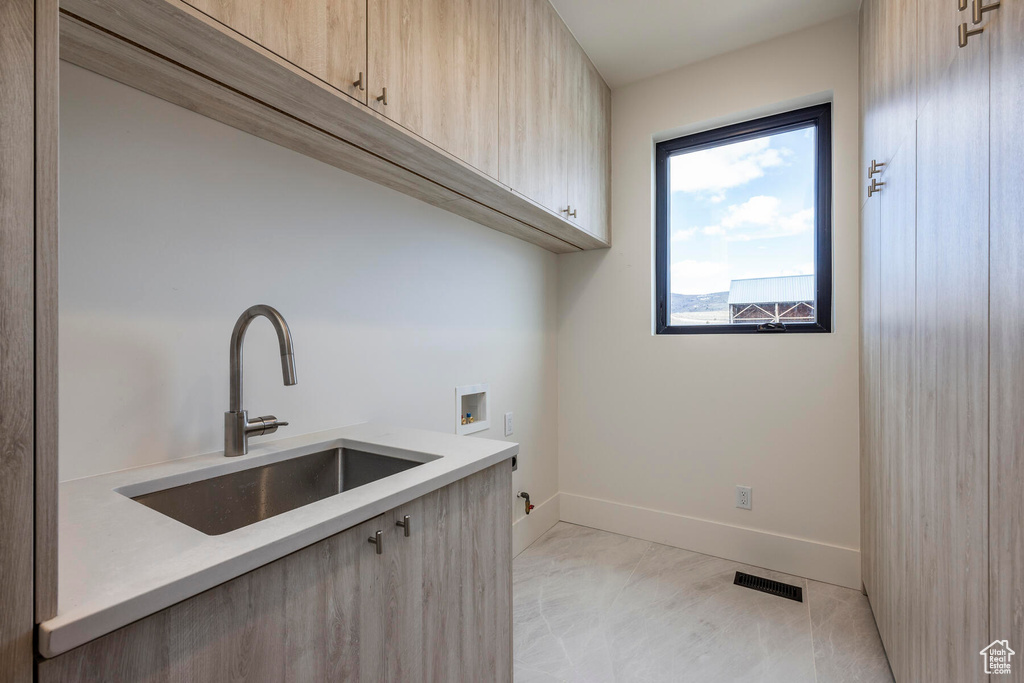 Clothes washing area featuring hookup for a washing machine, cabinets, and sink