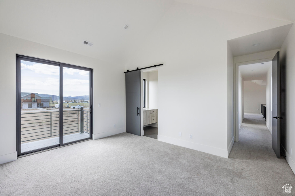 Unfurnished bedroom with a mountain view, a barn door, access to exterior, light colored carpet, and ensuite bathroom