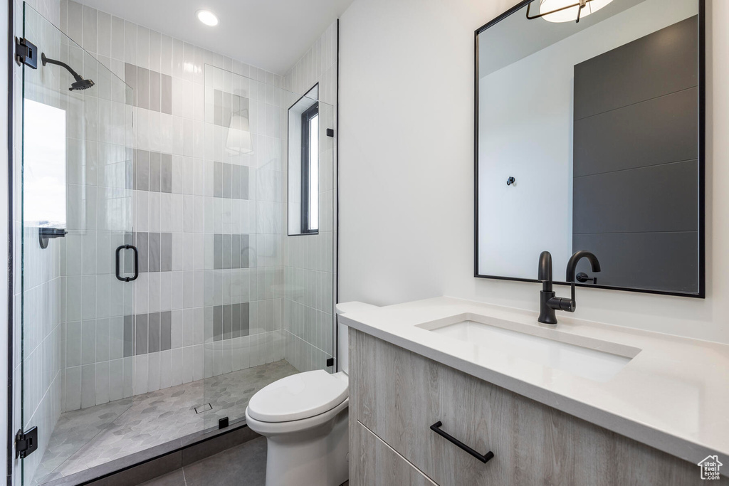 Bathroom with a wealth of natural light, vanity, a shower with shower door, tile patterned floors, and toilet