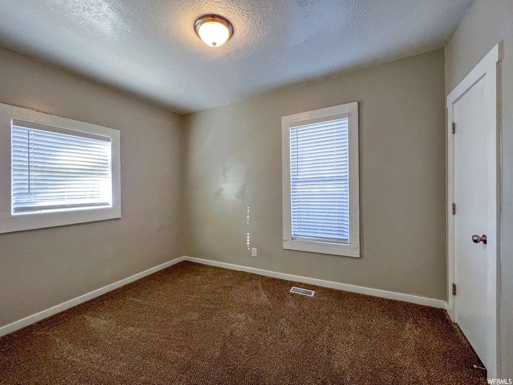 Spare room featuring plenty of natural light, a textured ceiling, and dark carpet