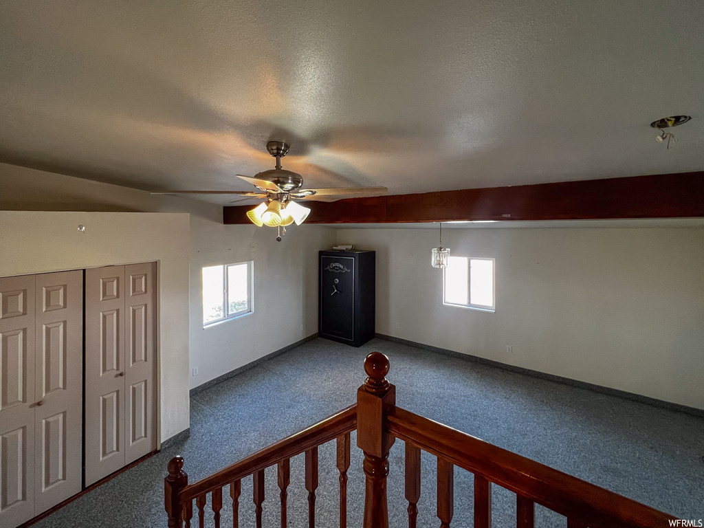 Carpeted spare room featuring plenty of natural light, ceiling fan, vaulted ceiling, and a textured ceiling
