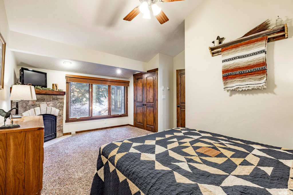 Carpeted bedroom with a fireplace, ceiling fan, and vaulted ceiling