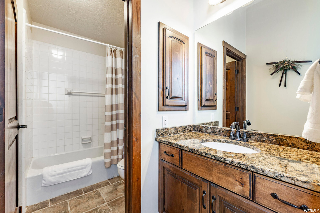 Full bathroom with tile flooring, vanity, a textured ceiling, toilet, and shower / tub combo