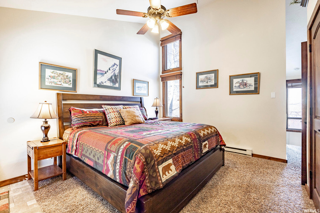 Carpeted bedroom with ceiling fan, baseboard heating, and high vaulted ceiling