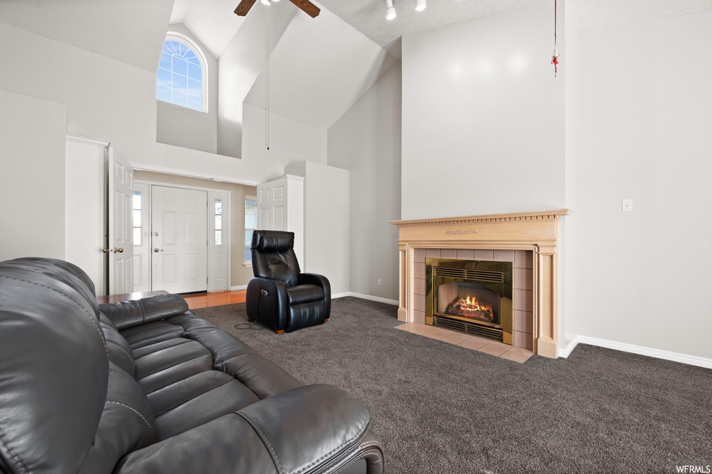 Carpeted living room with a fireplace, ceiling fan, and high vaulted ceiling