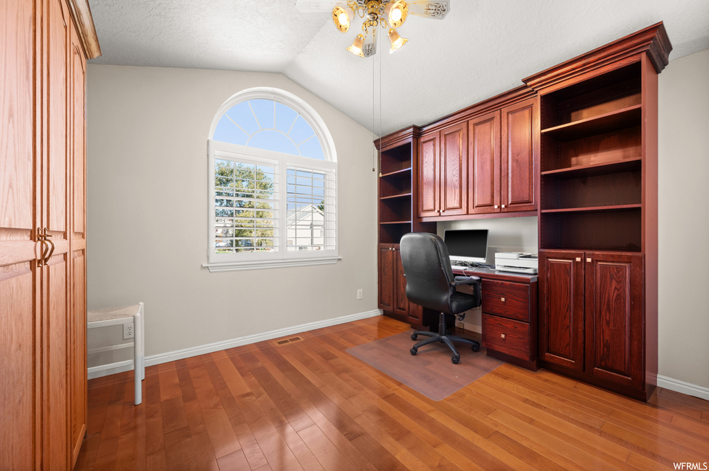 Office featuring light hardwood / wood-style floors, built in desk, ceiling fan, a textured ceiling, and lofted ceiling