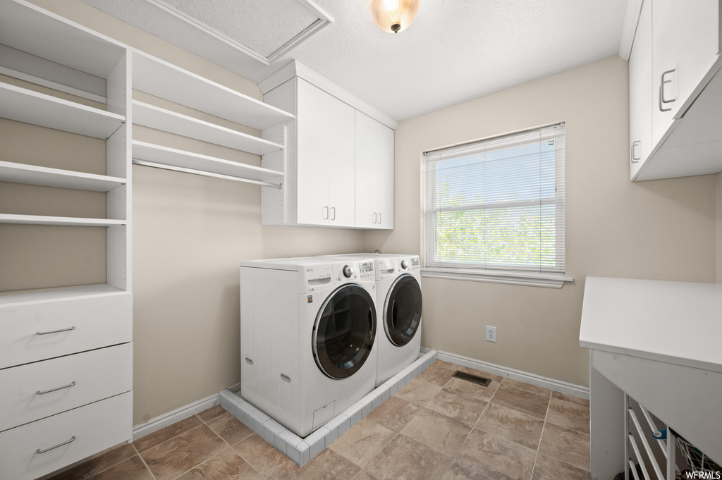 Washroom featuring washing machine and dryer, cabinets, and light tile floors