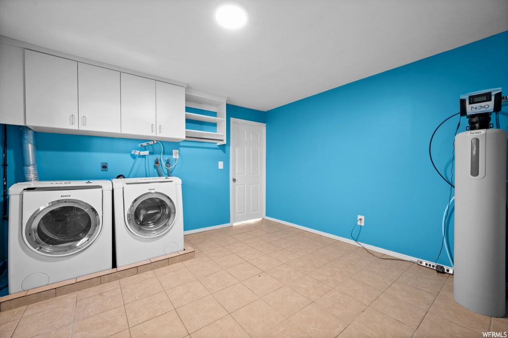 Laundry room featuring washing machine and clothes dryer, hookup for an electric dryer, hookup for a washing machine, light tile floors, and cabinets