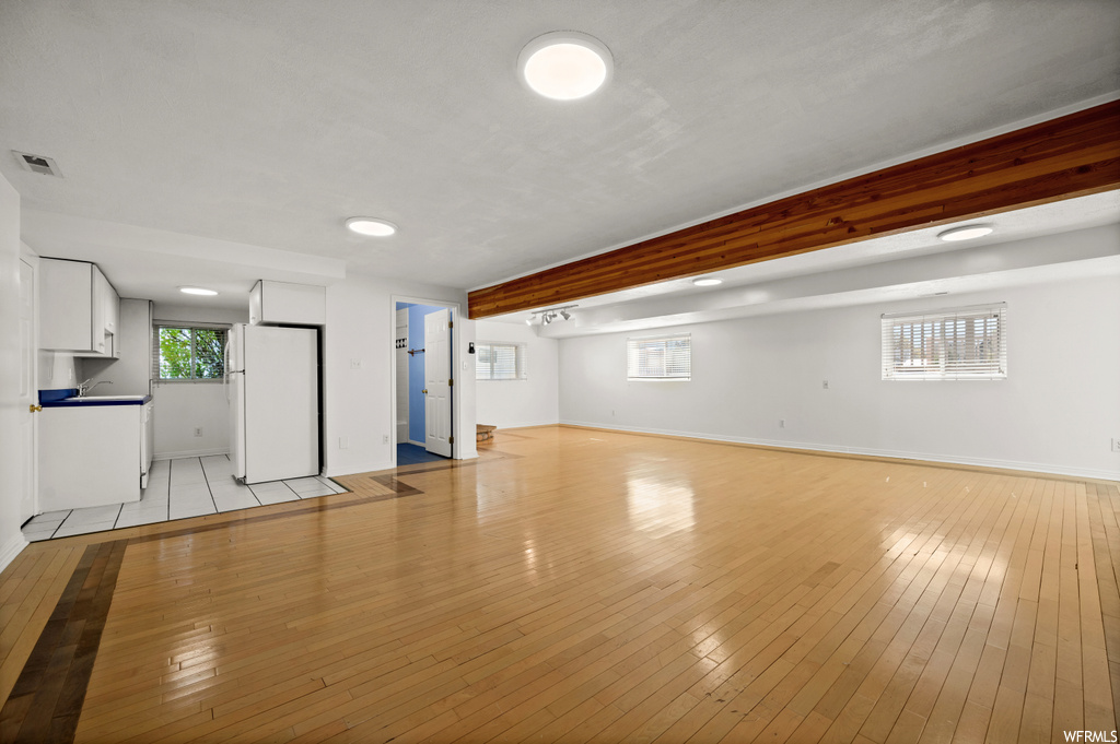 Unfurnished living room with light hardwood / wood-style floors and beamed ceiling
