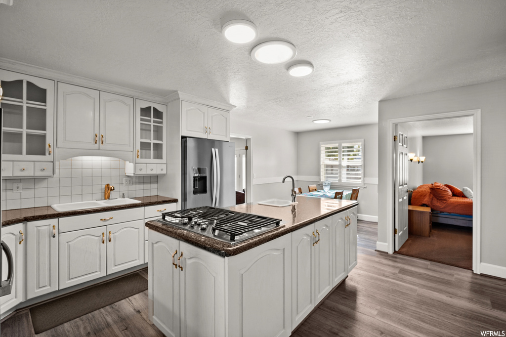 Kitchen featuring a center island with sink, backsplash, dark hardwood / wood-style flooring, stainless steel appliances, and white cabinetry