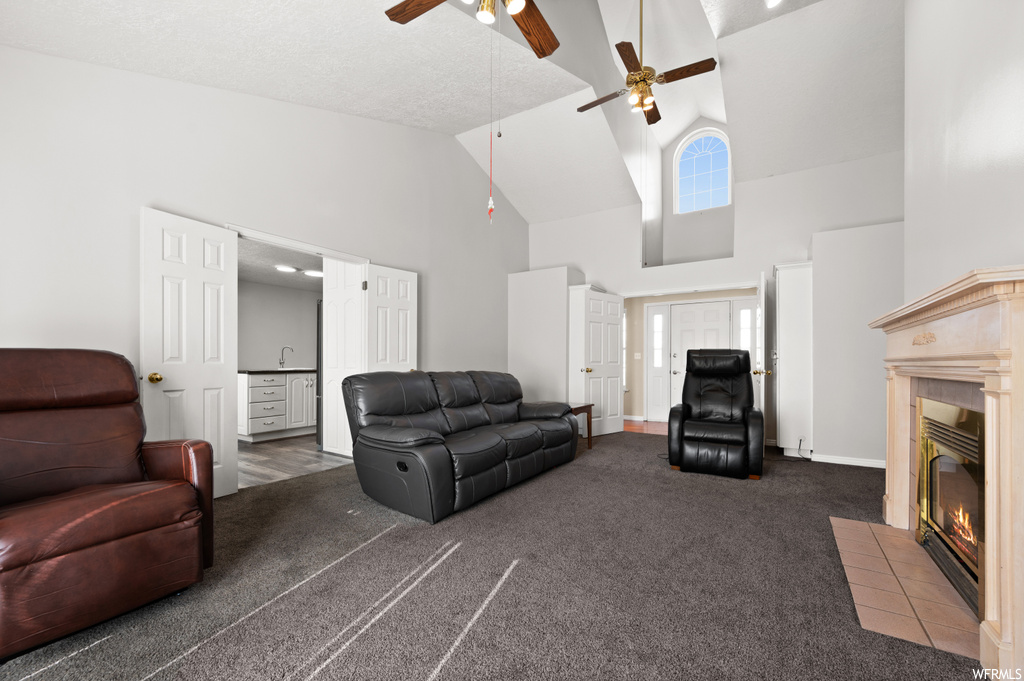 Living room featuring dark carpet, sink, high vaulted ceiling, ceiling fan, and a fireplace