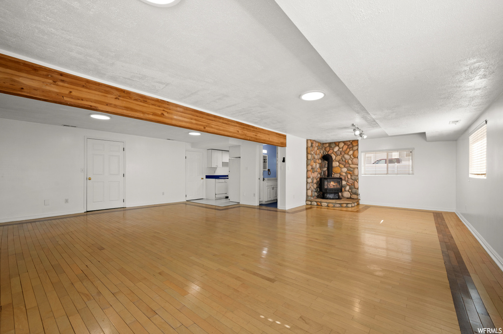 Basement featuring light hardwood / wood-style floors, a wood stove, and a textured ceiling