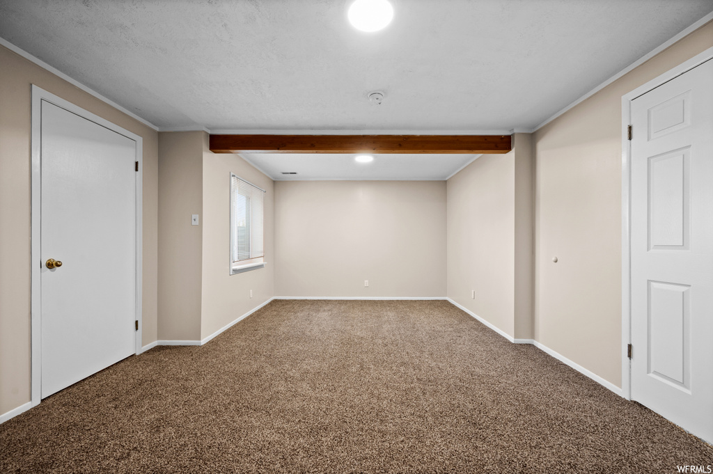 Spare room featuring carpet, a textured ceiling, beamed ceiling, and ornamental molding