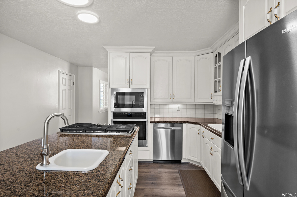 Kitchen with sink, backsplash, dark hardwood / wood-style flooring, white cabinetry, and dark stone counters