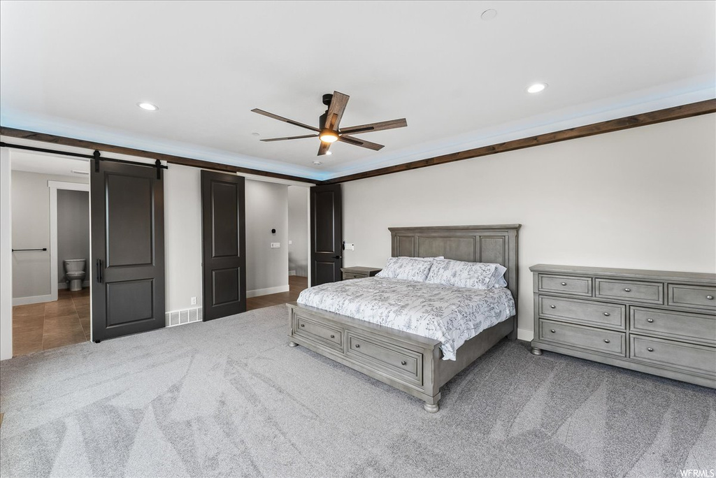 Bedroom featuring a barn door, light colored carpet, ceiling fan, and ornamental molding