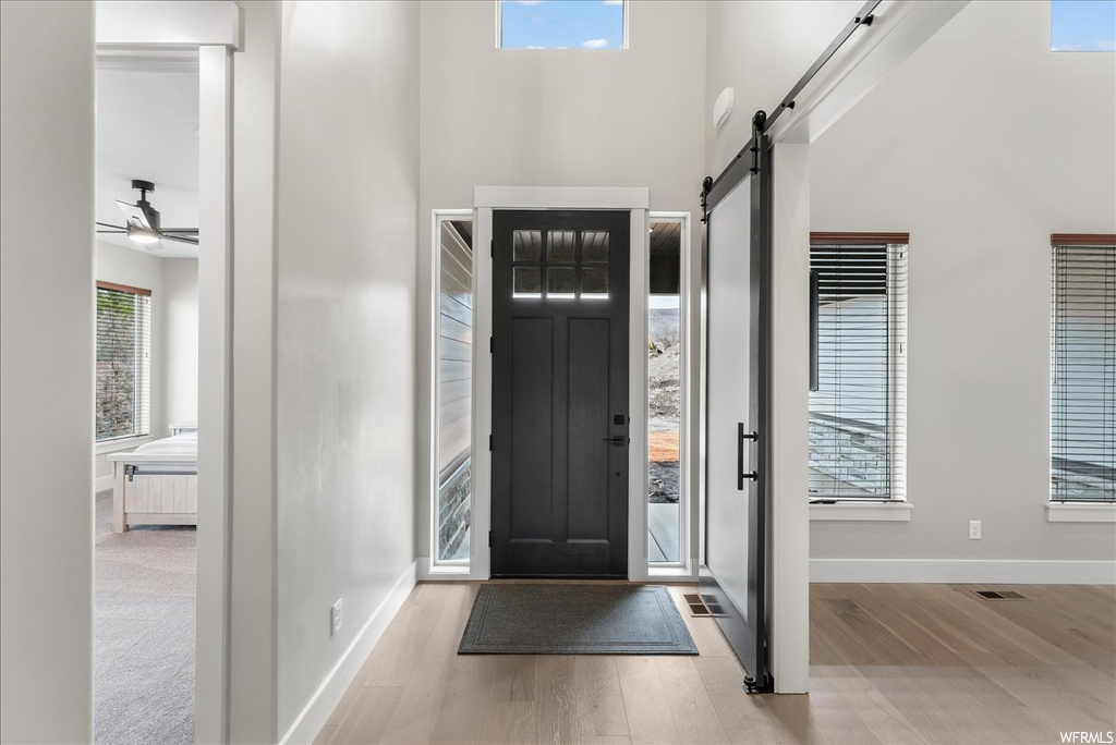 Foyer entrance with a barn door, ceiling fan, a towering ceiling, and light colored carpet
