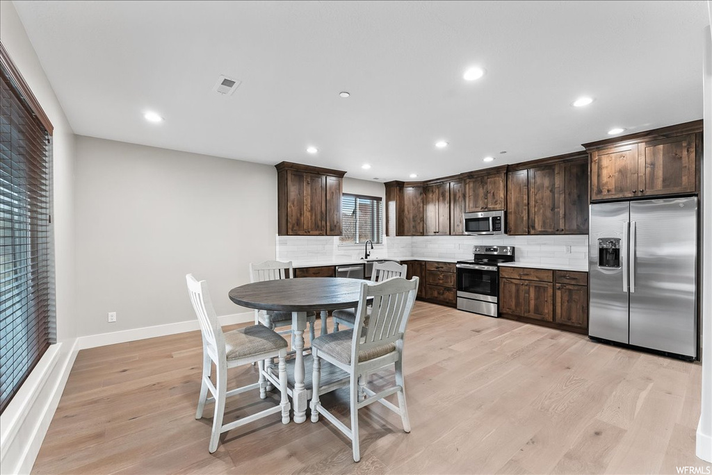 Kitchen featuring light hardwood / wood-style floors, backsplash, dark brown cabinets, and appliances with stainless steel finishes