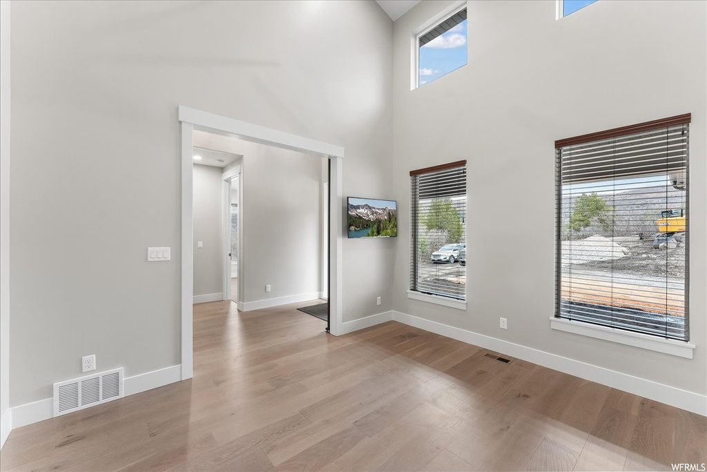 Spare room featuring light hardwood / wood-style floors, a towering ceiling, and a wealth of natural light