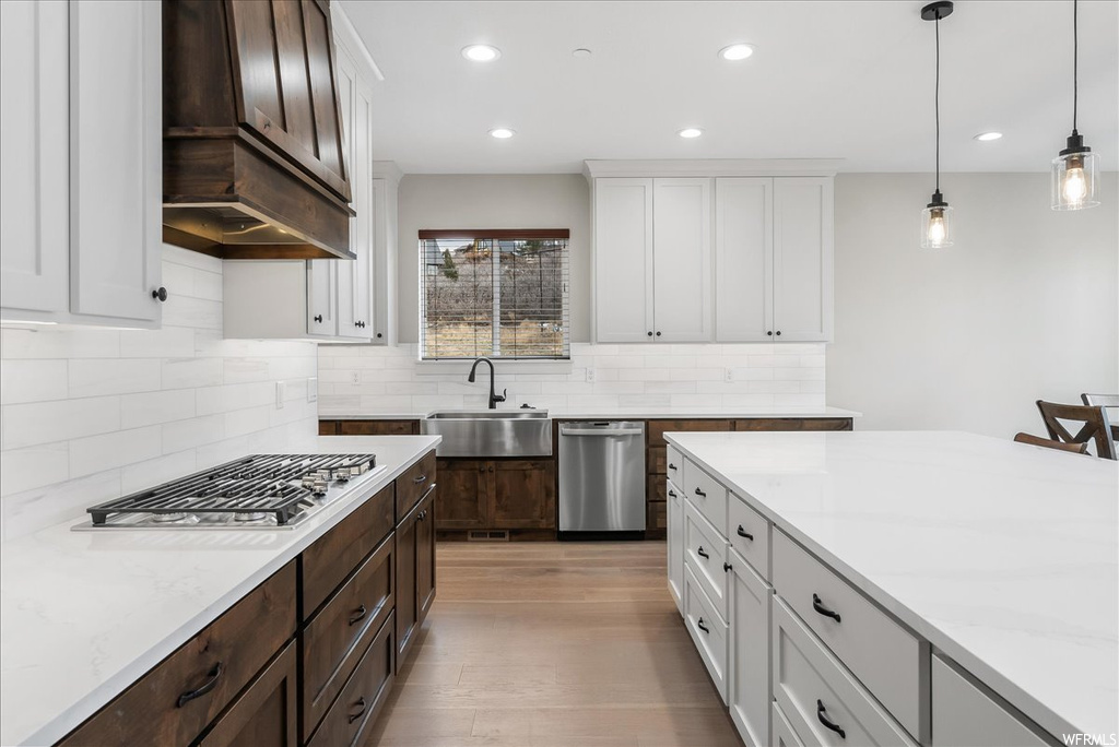 Kitchen with decorative light fixtures, custom exhaust hood, sink, light hardwood / wood-style flooring, and backsplash