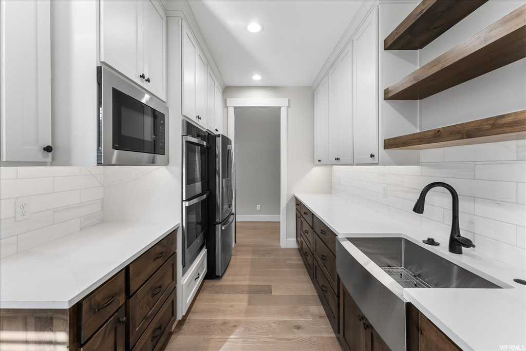 Kitchen featuring backsplash, stainless steel appliances, dark brown cabinets, white cabinetry, and light wood-type flooring