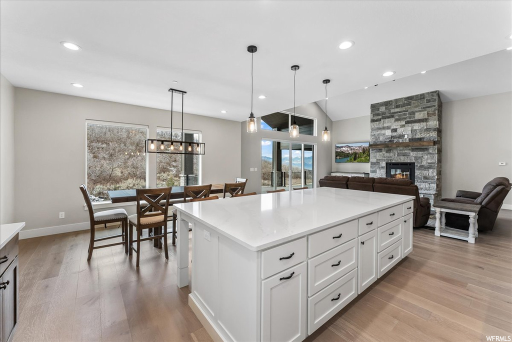 Kitchen with a kitchen island, a fireplace, light hardwood / wood-style floors, white cabinets, and pendant lighting