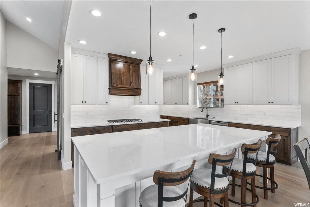 Kitchen featuring backsplash, decorative light fixtures, light wood-type flooring, and a center island