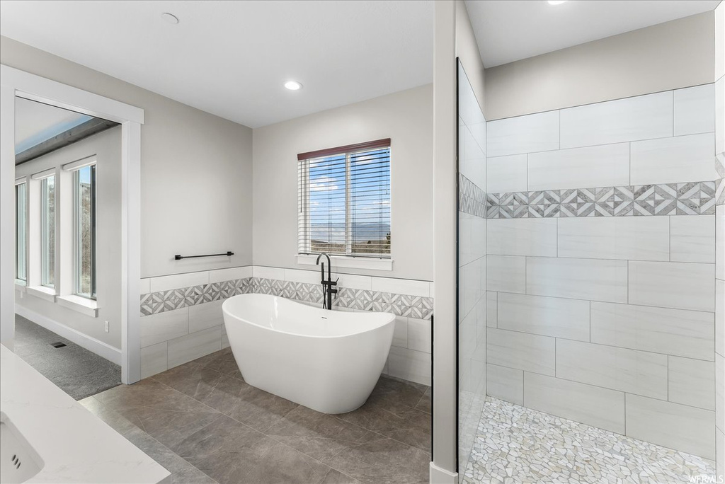 Bathroom featuring tile flooring, tile walls, a healthy amount of sunlight, and a bath