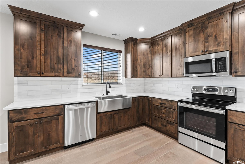 Kitchen with sink, light hardwood / wood-style floors, dark brown cabinetry, backsplash, and appliances with stainless steel finishes