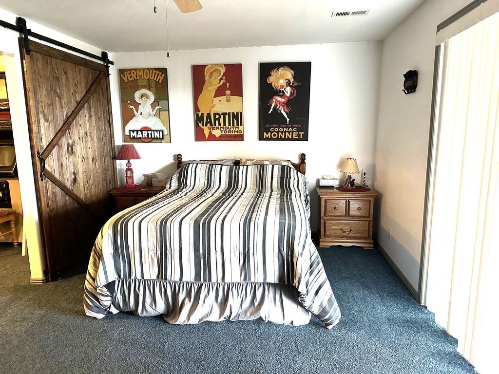 Bedroom featuring a barn door, dark carpet, and ceiling fan