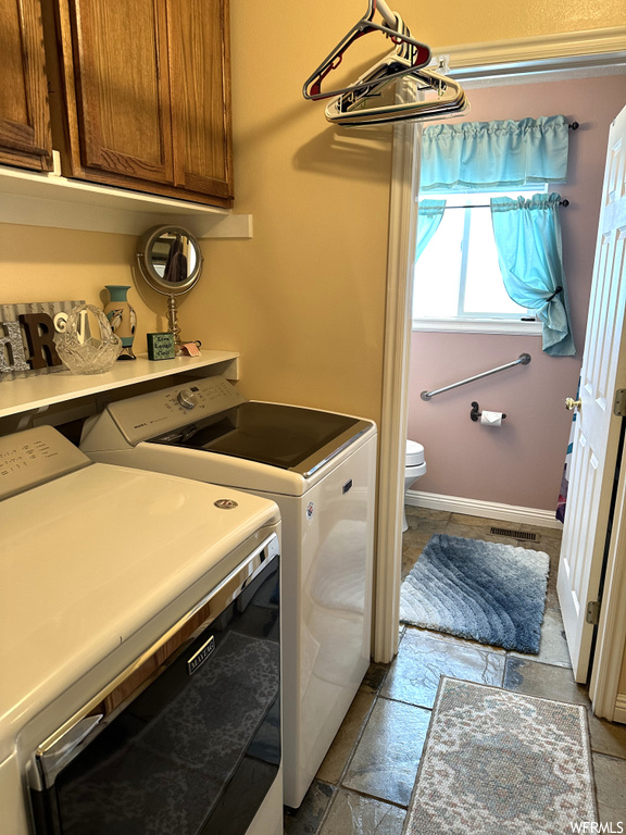 Laundry room featuring washing machine and clothes dryer, light tile floors, and cabinets