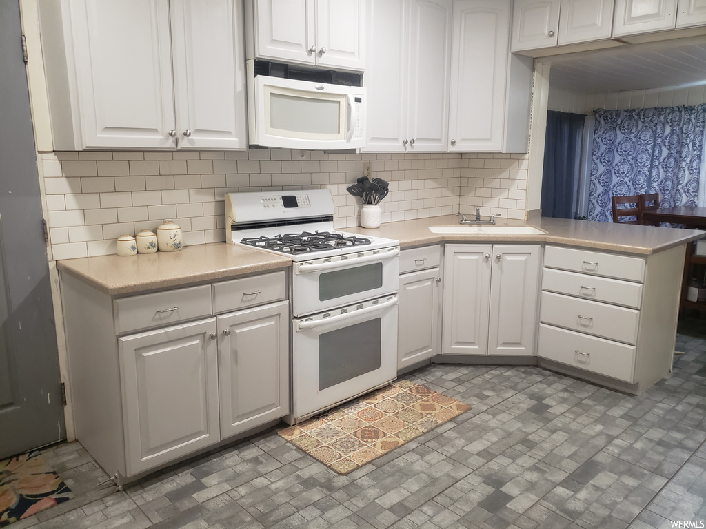Kitchen featuring tasteful backsplash, sink, dark tile flooring, white cabinets, and white appliances