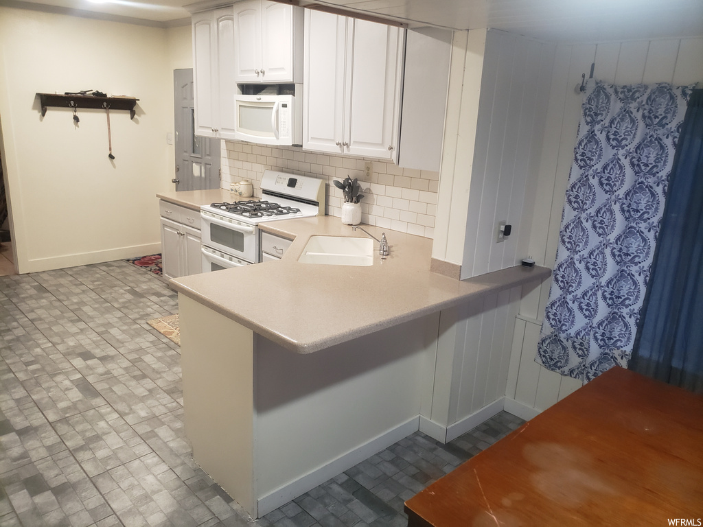 Kitchen with sink, dark tile floors, white appliances, backsplash, and white cabinetry