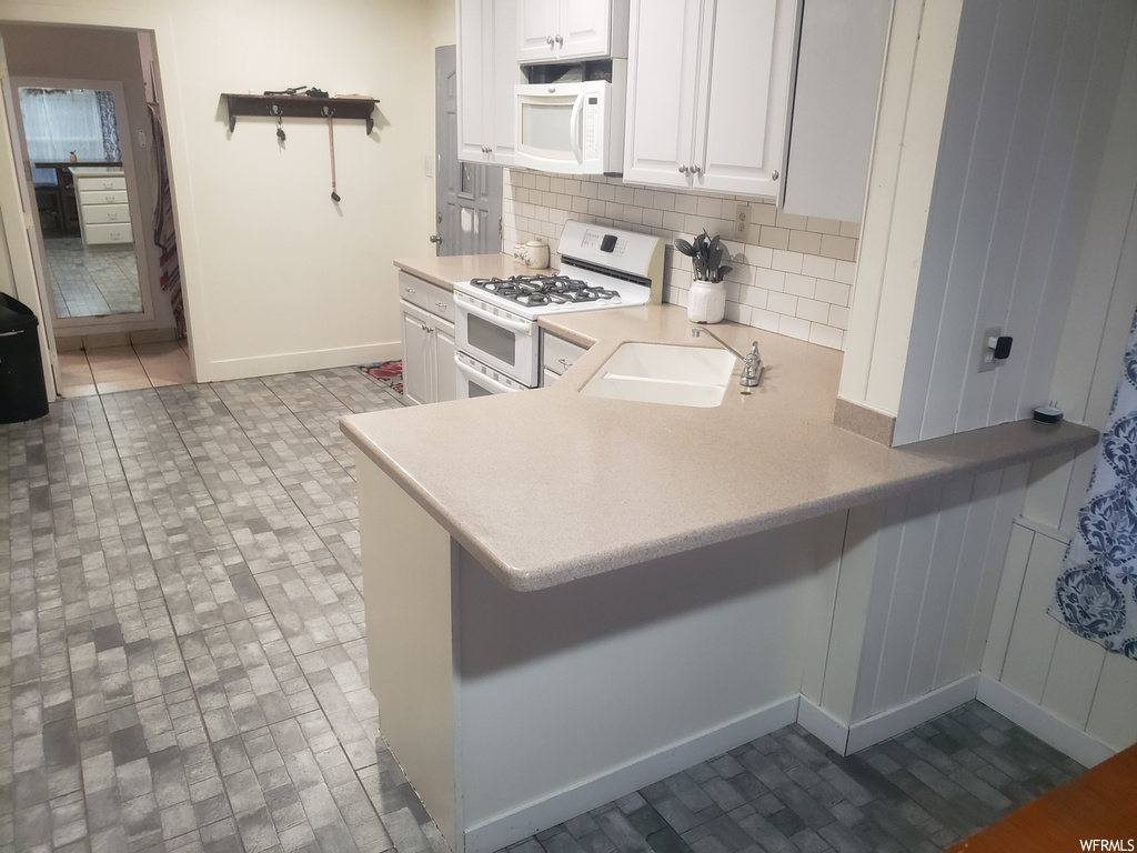 Kitchen featuring tasteful backsplash, tile flooring, sink, white cabinets, and white appliances
