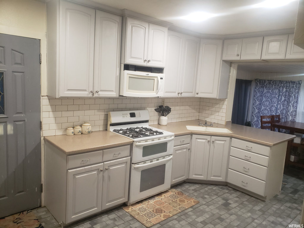 Kitchen featuring tasteful backsplash, sink, dark tile flooring, white cabinets, and white appliances