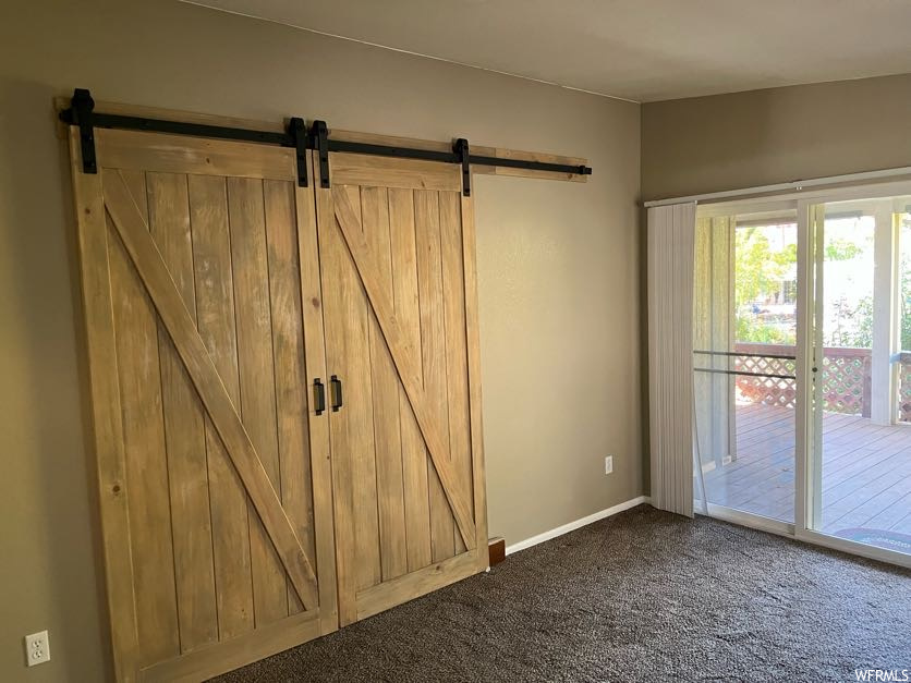 Unfurnished bedroom with a barn door, dark carpet, and access to outside