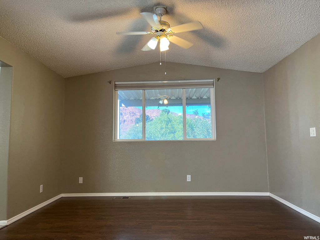 Empty room with vaulted ceiling, ceiling fan, dark hardwood / wood-style floors, and a textured ceiling