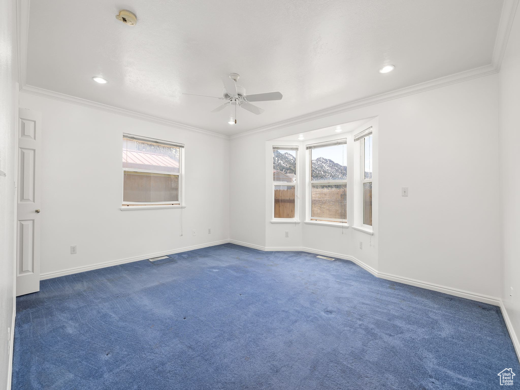 Empty room featuring crown molding, ceiling fan, dark colored carpet, and plenty of natural light