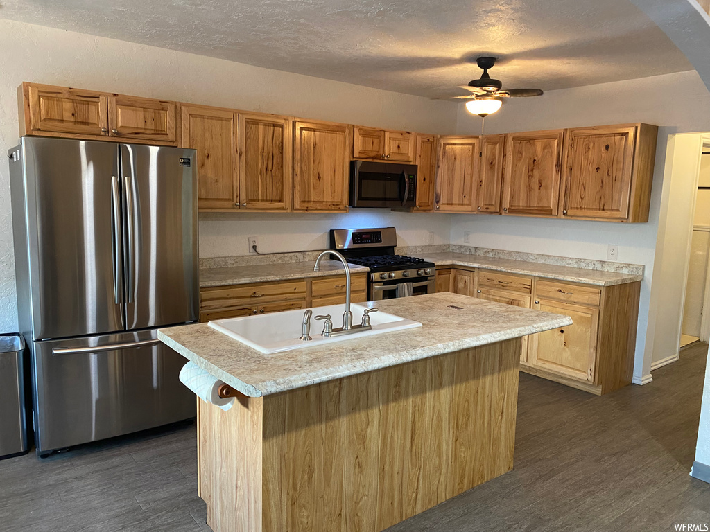 Kitchen with sink, a kitchen island with sink, a textured ceiling, stainless steel appliances, and ceiling fan