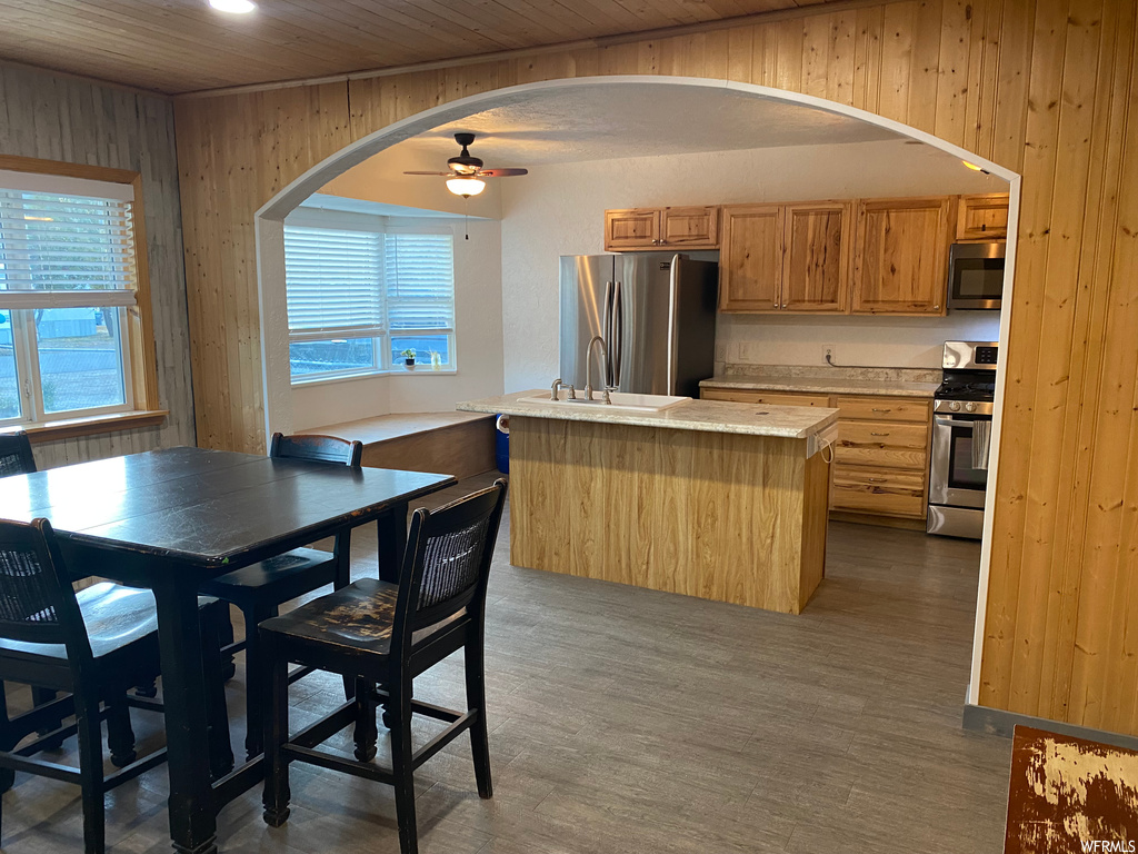 Kitchen featuring light hardwood / wood-style floors, a center island, wooden walls, appliances with stainless steel finishes, and ceiling fan