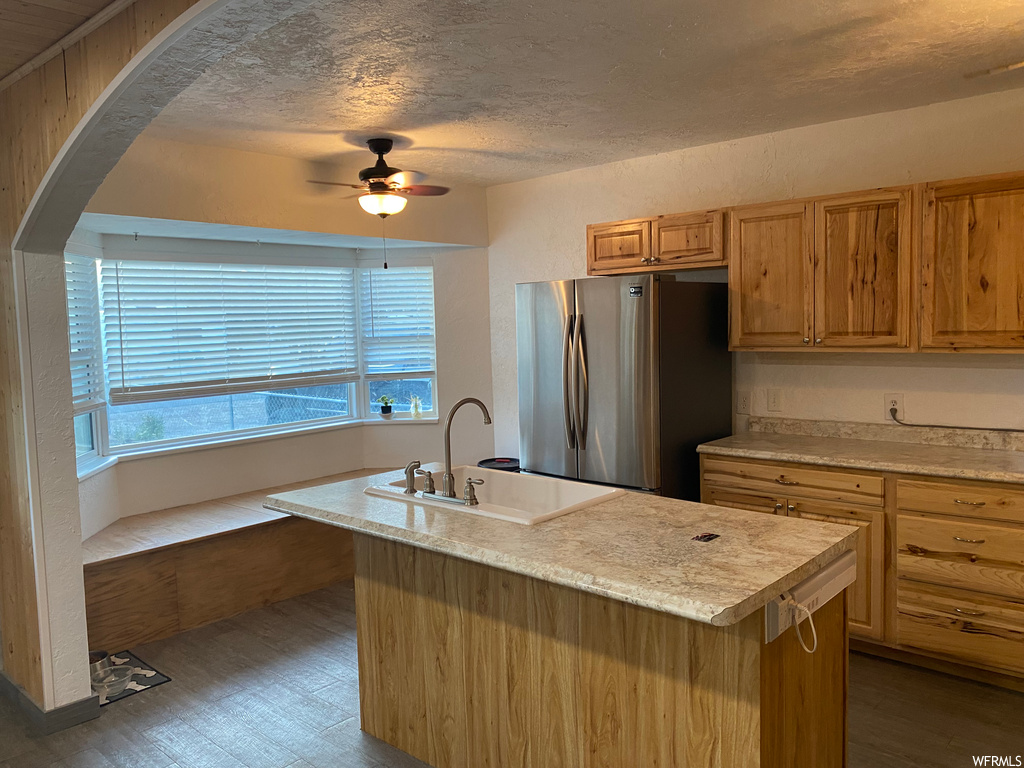 Kitchen featuring a center island with sink, stainless steel refrigerator, hardwood / wood-style flooring, and ceiling fan